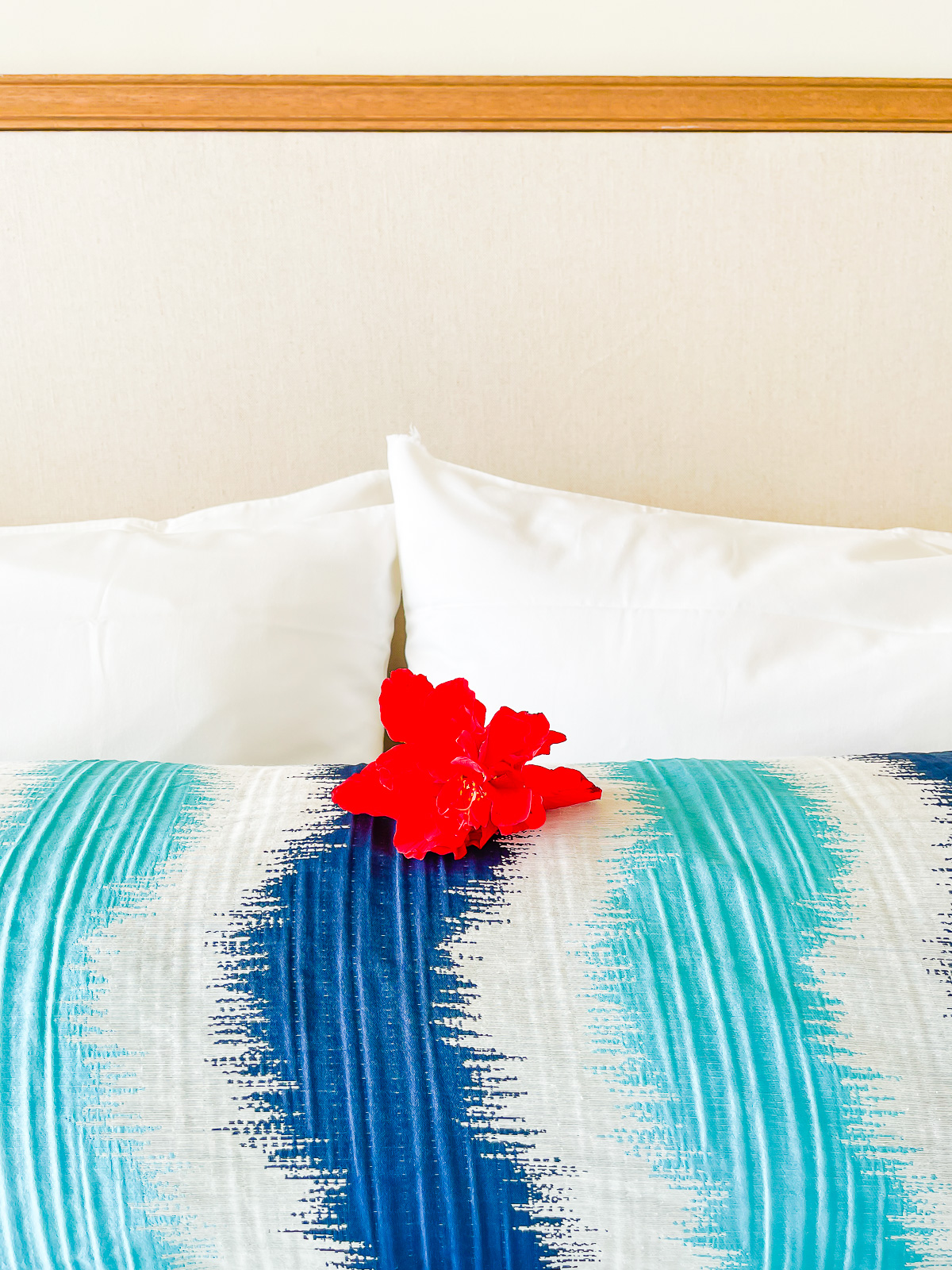bright red hibiscus flower on hotel room bed.