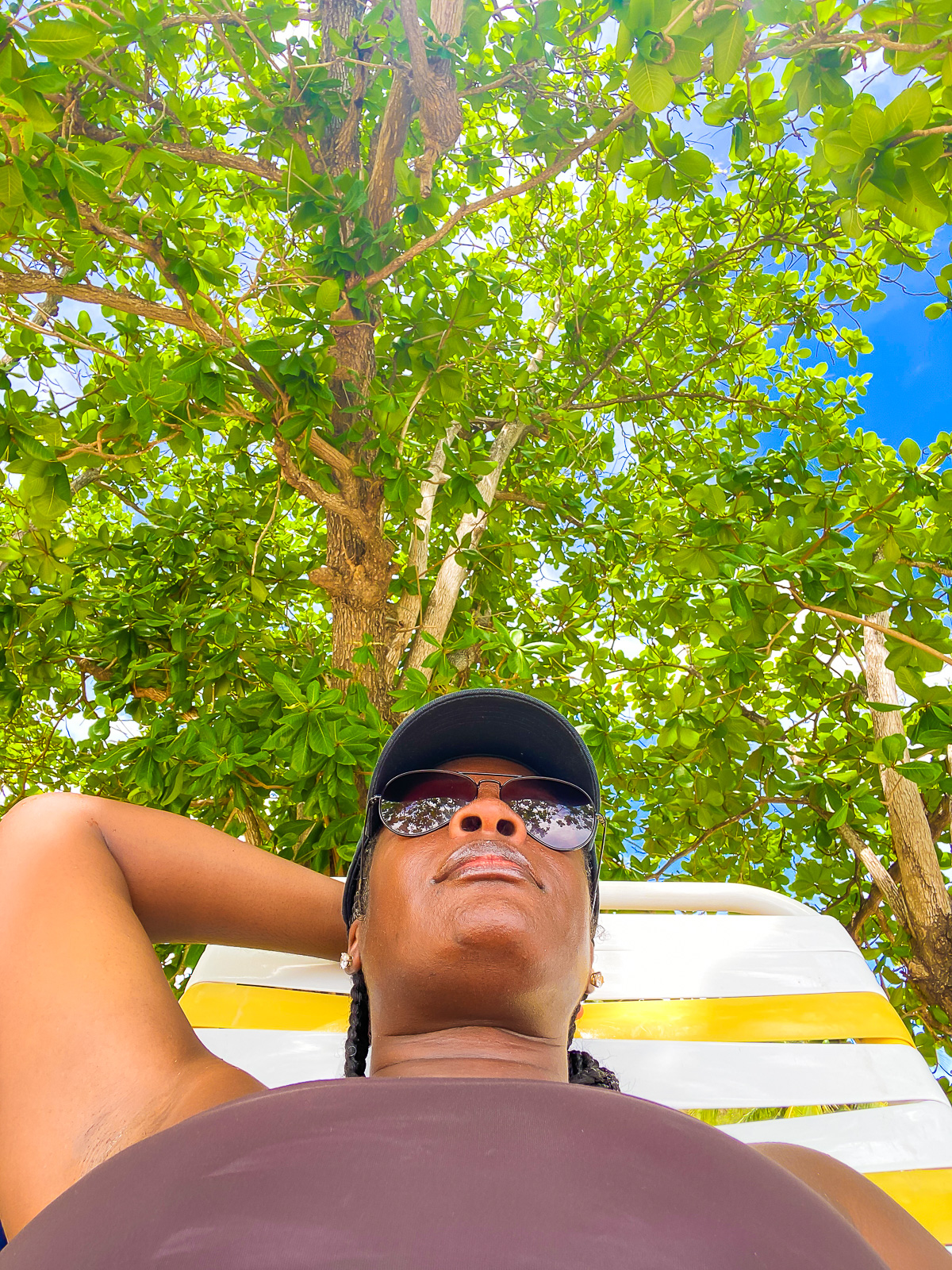 Jazzmine reclined in a yellow and white striped beach chair underneath a lush mango tree on BBC Beach, Grenada.