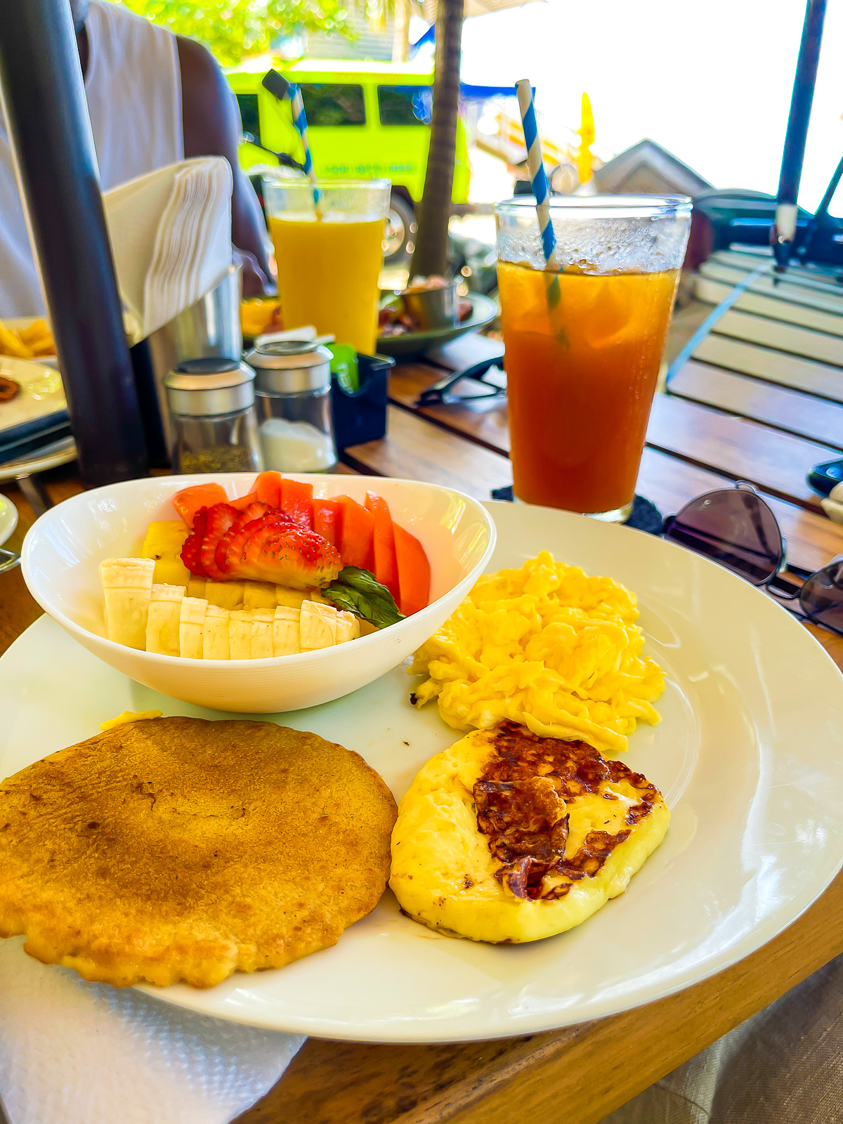 breakfast plate at Pico Bistro with fresh sliced papaya, pineapple, strawberry, and banana, Costa Rican fry bread, cheese, and scrambled eggs next to a Tamarindo agua fresca.