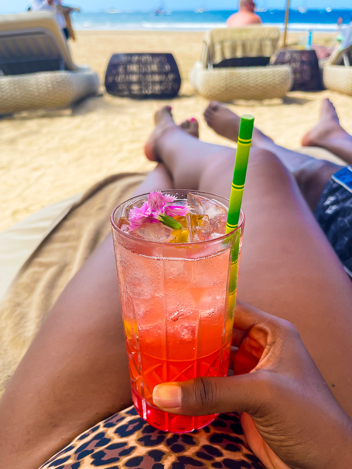 brown hand holding a bright red drink in a beach lounger at Tamarindo Beach.