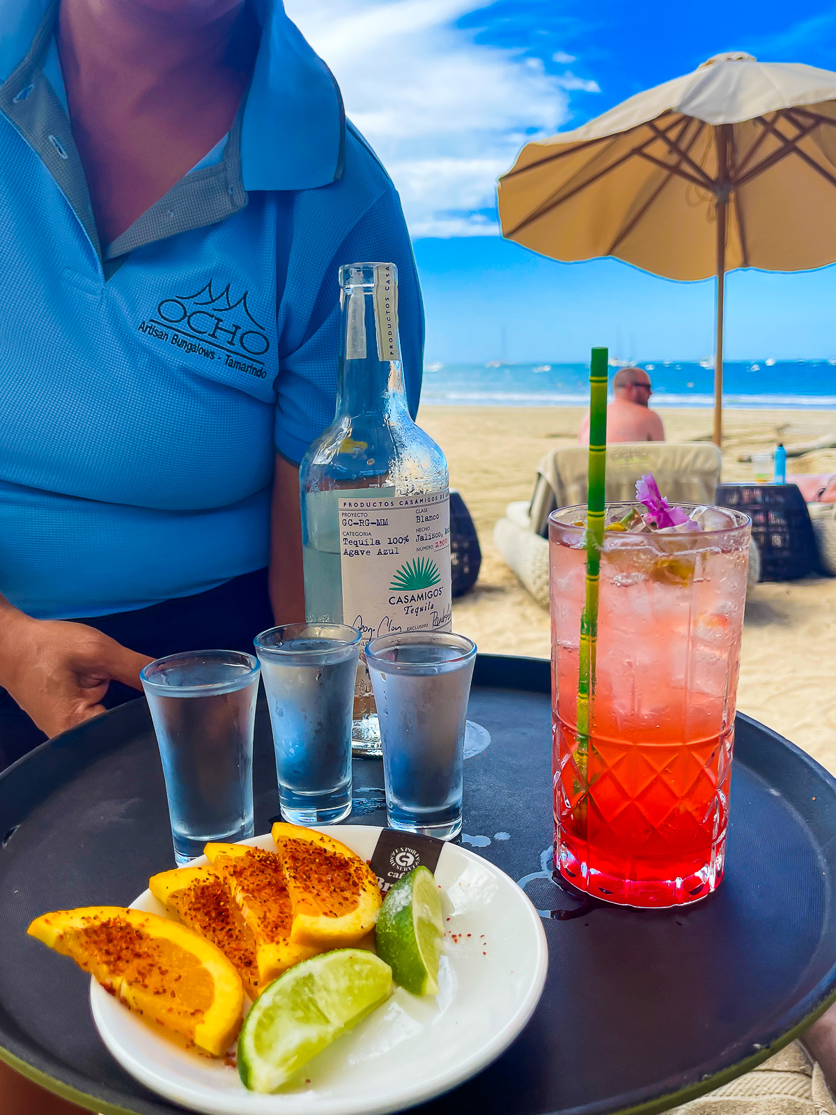 server holding a platter of tequila shots, citrus wedges, and a flamingo mocktail at Tamarindo's Ocho Beach Club.