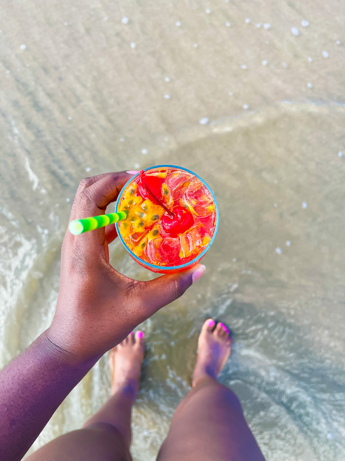 Jazzmine holding a bright red mocktail with maraschino cherries and fresh passion fruit on the beach.