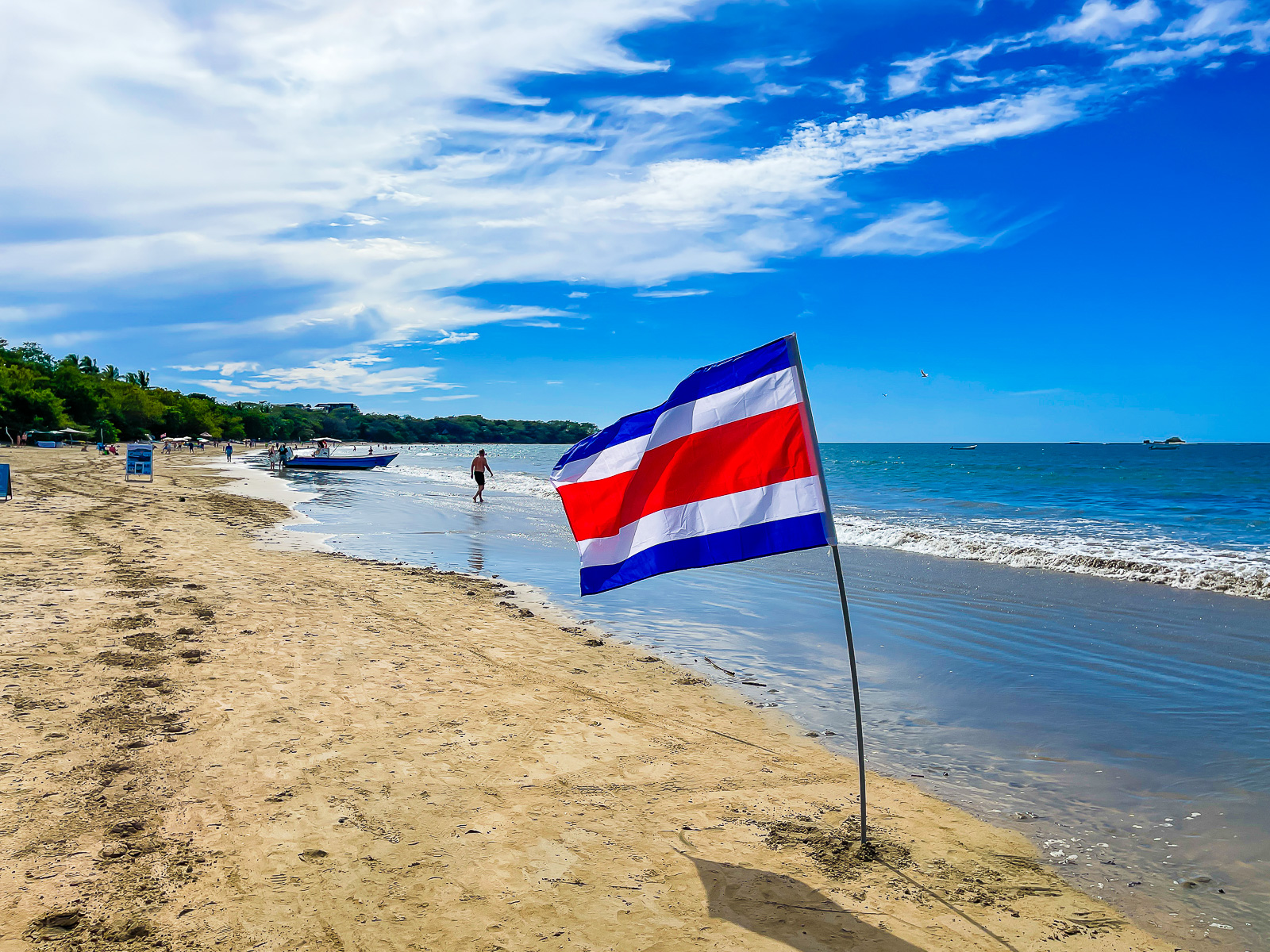 blue white and red Costa Rican flag planted in the sand near the shoreline of Tamarindo Beach.